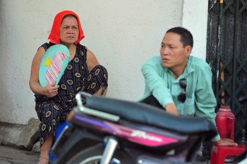 Ngồi trên vỉa hè, cụ bà này đầu đội khăn ướt, tay không ngừng phe phẩy quạt.