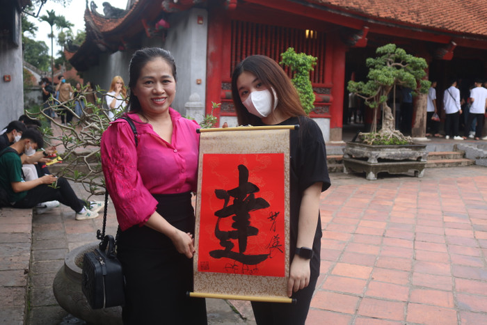 Phụ huynh học sinh Nguyễn Phương Anh (đứng bên trái) cho biết: "Bản thân tôi cũng hồi hộp, lo lắng như các con, không biết đề thi có vừa sức với các con hay không". Chị và con gái xin chữ "Đỗ Đạt" để mong con thi đỗ vào Trường Đại học Luật Hà Nội