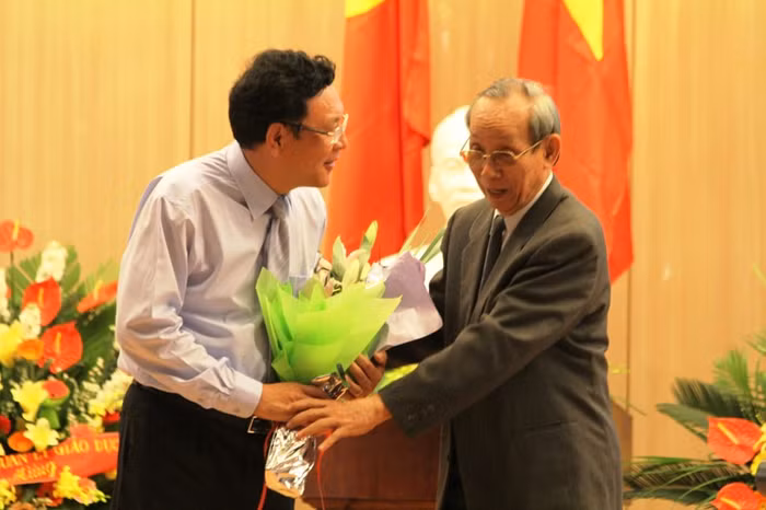 Bộ trưởng Bộ GD&amp;ĐT Phạm Vũ Luận nhận hoa từ GS. Trần Hồng Quân - Chủ tịch Hiệp hội các trường Đại học, Cao đẳng Việt Nam trong một hội nghị. Ảnh Xuân Trung