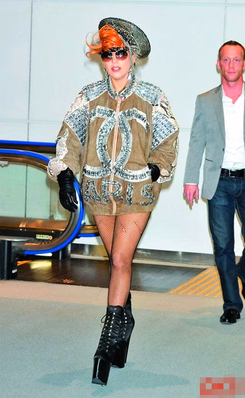 Chiếc áo của thương hiệu Chanel được Lady Gaga phối thành một chiếc váy, đầu đội mũ lệch lộ màu tóc đỏ cam, đeo găng tay và đi boot cao chót vót.