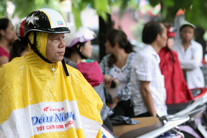 Gần tới giờ làm bài cũng là lúc cơn mưa rào bất chợt đổ xuống, kiên nhẫn mặc áo mưa chờ con.