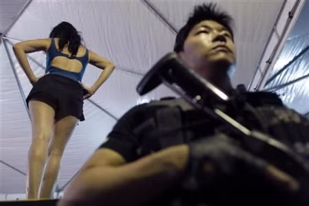 Một cảnh sát đang đứng làm nhiệm vụ tại nhà tù nữ giới Brasilia, Brazil. Sau lưng cảnh sát này là một nữ tù binh, ăn mặc rất “thoải mái”.