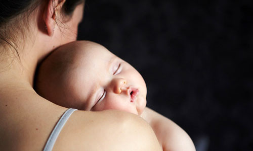 Thay vì để bé ngủ say trong vòng tay bạn rồi mới đưa vào cũi, hãy cho bé vào giường khi còn đang mơ màng. Ảnh: Inmagine.