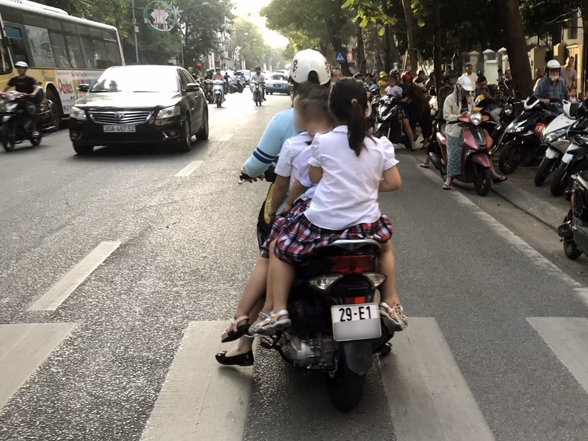 Trước cổng Trường tiểu học Phan Chu Trinh, phụ huynh đi ngược chiều và không đội mũ bảo hiểm cho 3 trẻ. Ảnh: Tùng Dương.