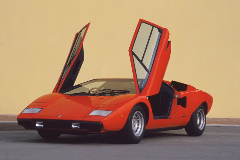 2. Lamborghini Countach (1974 - 1990) Countach là mẫu xe thể thao động cơ đặt giữa được Lamborghini đưa vào sản xuất trong khoảng thời gian từ năm 1974 đến 1990. Đây có thể xem là mẫu xe tiên phong và định hình phong cách hầm hố, góc cạnh của các dòng xe Lamborghini nói riêng và siêu xe nói chung. Thiết kế đẩy cabin lái về phía trước nhằm tăng diện tích cho động cơ, và đặc biệt là cửa ra vào đóng mở kiểu cắt kéo cũng từ chính Countach mà ra. Cái tên Countach bản thân nó cũng có một "tiểu sử" thú vị riêng. Đây là một từ cảm thán trong ngôn ngữ địa phương tại Ý có tên Piedmontese, thường được sử dụng bởi nam giới mỗi khi nhìn thấy một người phụ nữ tuyệt đẹp. Những lô Countach đầu tiên sử dụng chung động cơ V12 4 lít của Miura, sau này được nâng cấp lần lượt lên 5 lít rồi 5,2 lít. Có cả thảy 5 phiên bản Countach được sản xuất, bao gồm LP400, LP400S, LP500S, LP5000QV và một phiên bản đặc biệt nhân kỷ niệm 25 năm Countach ra đời. Tổng cộng, Lamborghini đã chế tạo được 2.042 chiếc Countach trong vòng đời 16 năm của nó. Cái tên Countach chỉ bị lu mờ phần nào kể từ khi kẻ kế nhiệm nó xuất hiện, Lamborghini Diablo.