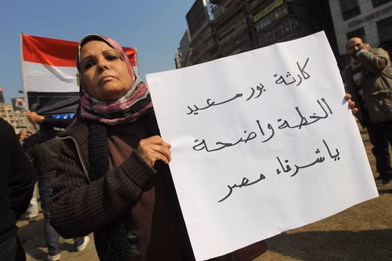 Một người khác giơ biểu ngữ: “Thảm họa Port Said: đó rõ ràng là một sự dàn xếp”.