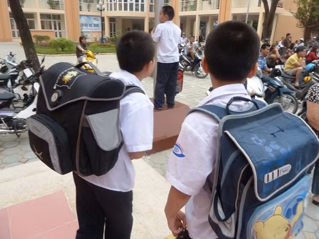 Trẻ con oằn lưng cõng cặp tới trường.