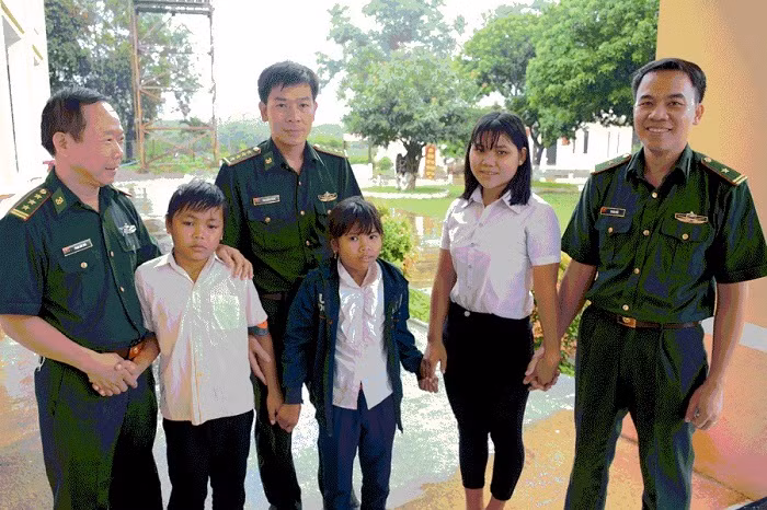 Những em học sinh được nhận làm con nuôi tại Đồn Biên phòng Ia O (Gia Lai). Theo Đại úy Phan Công Thắng (đứng thứ ba từ trái qua phải) riêng với trường hợp của Siu H’Ly, mỗi tháng đơn vị hỗ trợ khoảng 900 ngàn đồng; còn đối với Rơ Lan H’Ly và Kpuih Hiếu, đơn vị trích kinh phí hỗ trợ 500 ngàn đồng/cháu/tháng. Sắp tới, đơn vị cũng sẽ trích một phần kinh phí mua sách vở, áo quần, dụng cụ học tập… để các cháu bước vào năm học mới. Ảnh Phương Dung