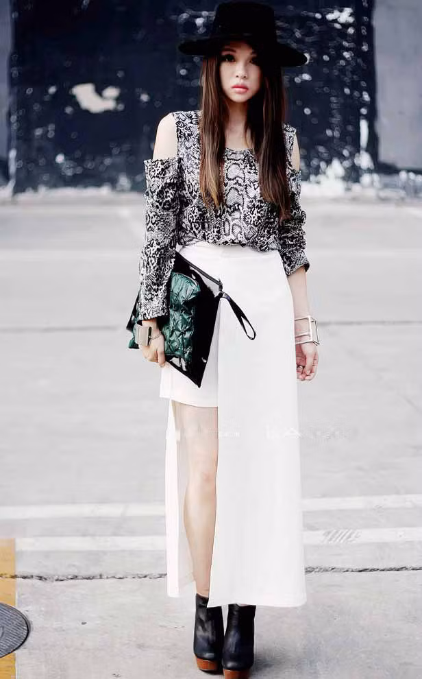 Một chiếc váy dài màu trắng với những đường xẻ phá cách làm nổi bật chiếc áo họa tiết da rắn sang trọng và quyến rũ.