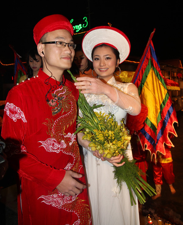 Là đạo diễn cho màn rước dâu bằng thuyền rồng nên Ngọc Linh phải đeo tai nghe để "chỉ đạo" mọi người. Khi thuyền đã cập bến, Diệu Hương nhắc ông xã tháo tai nghe để chuẩn bị cho nghi lễ tiếp theo. Ảnh: Quỳnh Như, Ngôi sao