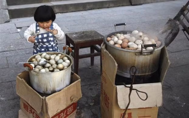 Một bé gái đang nhìn chằm chằm vào nồi trứng luộc bằng nước bình thường bên cạnh nồi trứng luộc bằng nước tiểu của các bé trai tại Dongyang ngày 26/3/2012 Một bé gái đang nhìn chằm chằm vào nồi trứng luộc bằng nước bình thường bên cạnh nồi trứng luộc bằng nước tiểu của các bé trai tại Dongyang ngày 26/3/2012