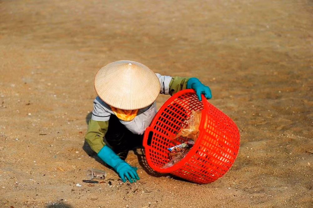 Đội công nhân vệ sinh thu dọn rác từ khách du lịch để lại trên bãi cát.
